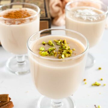 three glasses of thick milk drink topped with pistachio, cinnamon or coconut