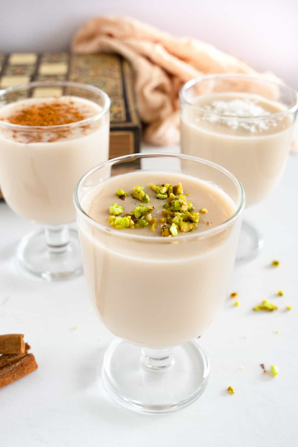 three glasses of thick milk drink topped with pistachio, cinnamon or coconut