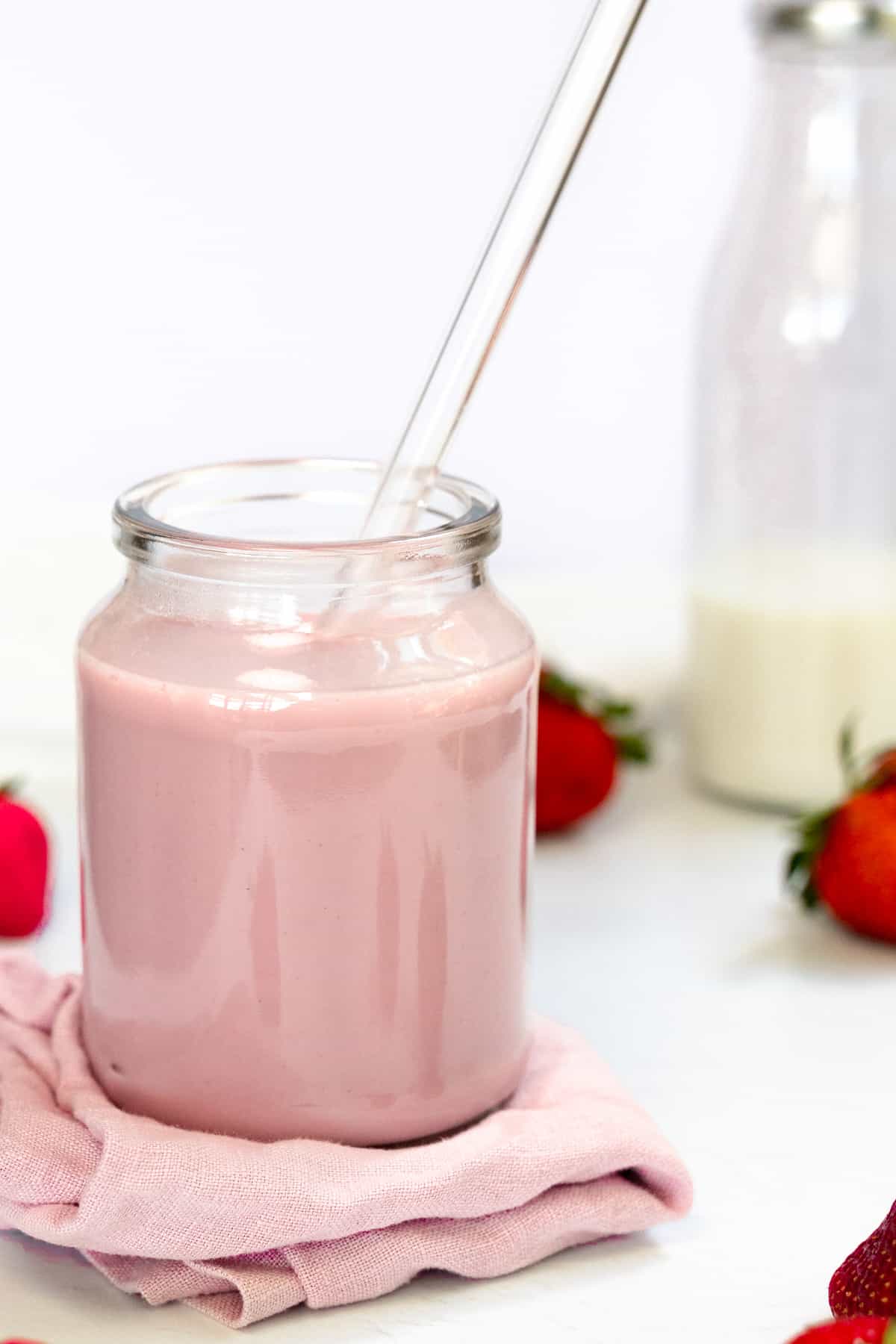 a glass jar with a glass straw filled with pink milk