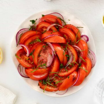 a white plate filled with sliced tomato and onion salad with spices and seasoning on the side