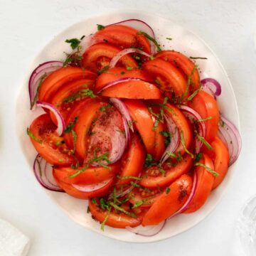 a white plate filled with sliced tomato onion salad with specks of green herbs