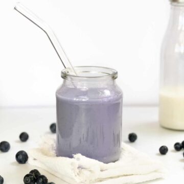 a glass jar with a glass straw filled with purple milk