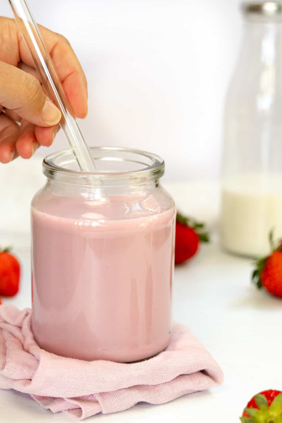 a hand holding a glass straw in a glass jar with pink milk in it