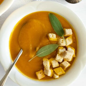 a white bowl with orange soup topped with croutons and a pepper shaker on the side