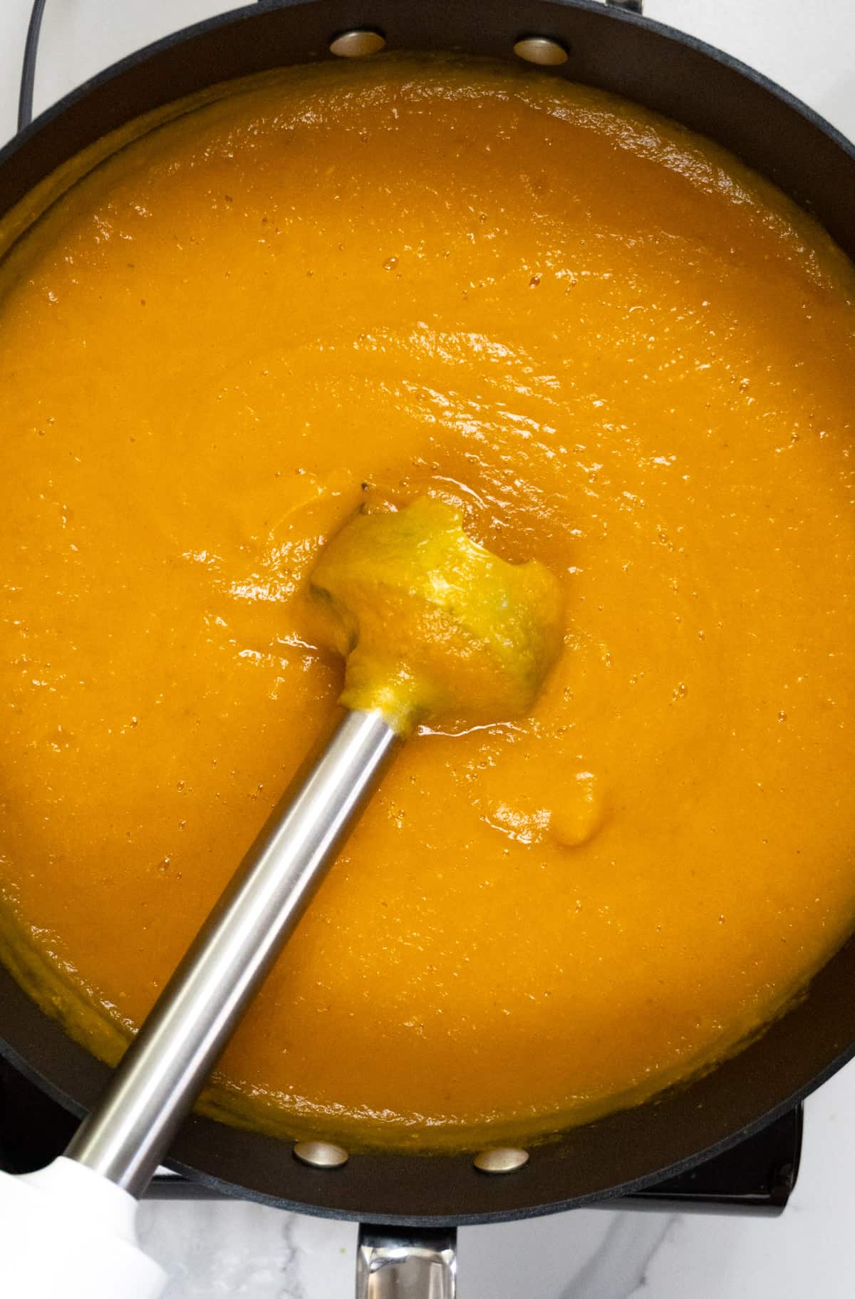 blended orange soup with an immersion blender in it