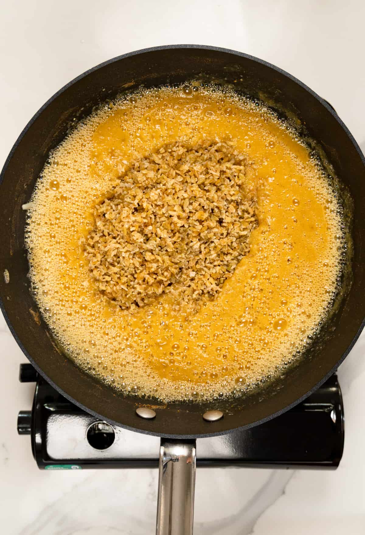 adding soaked freekeh grain to a pot of blended thick yellow broth