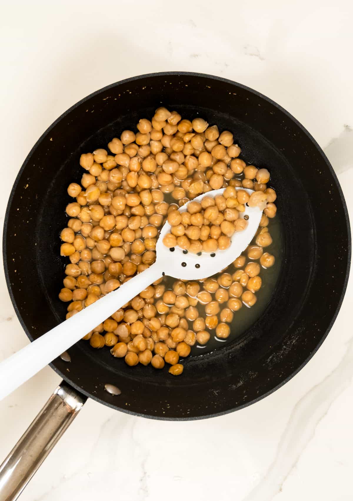 boiled chickpeas with a white slotted spoon in a black pot