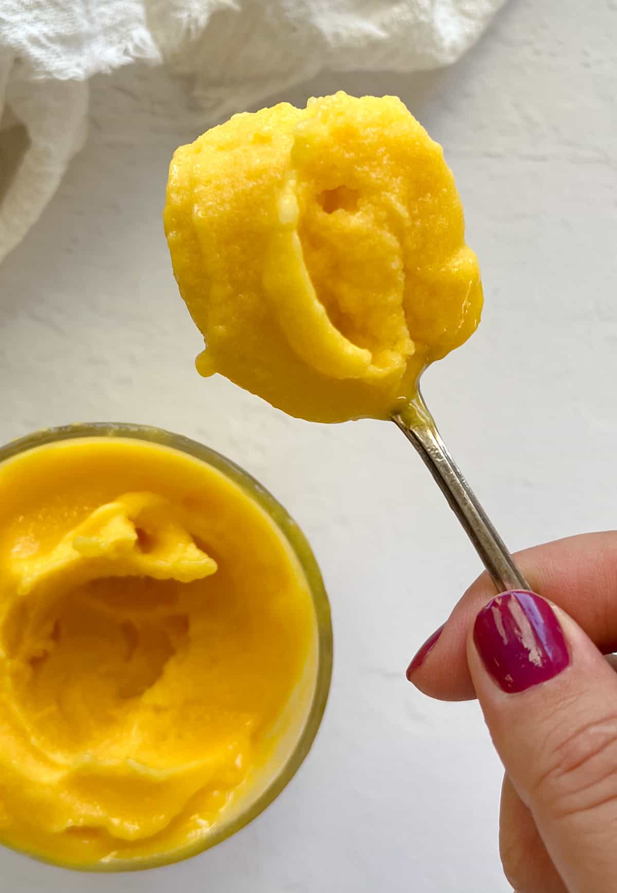 a female hand with fuscia painted nails holding a spoonful of sorbet