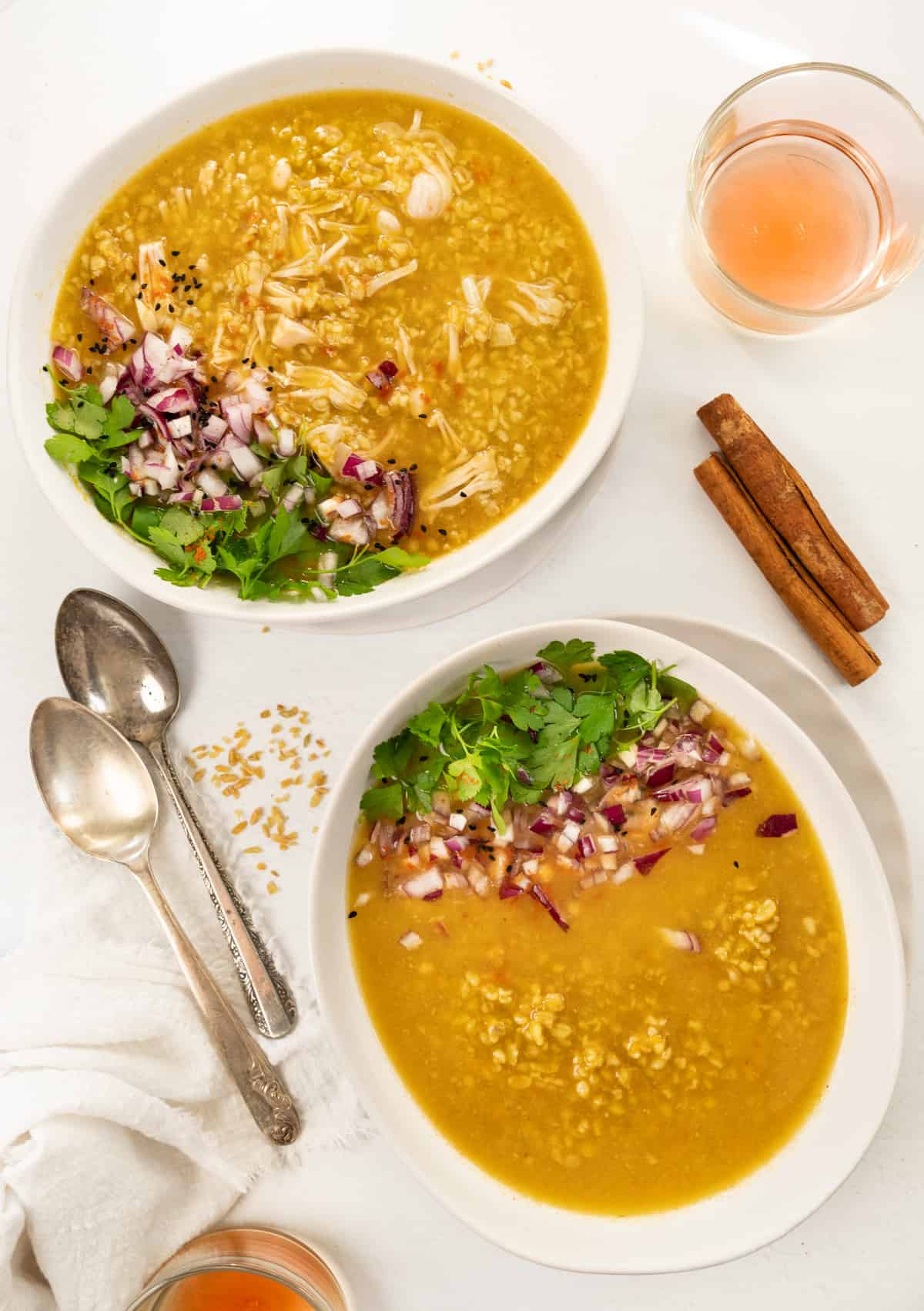 two bowls of thick yellow grain soup garnished with green herbs and diced red onion