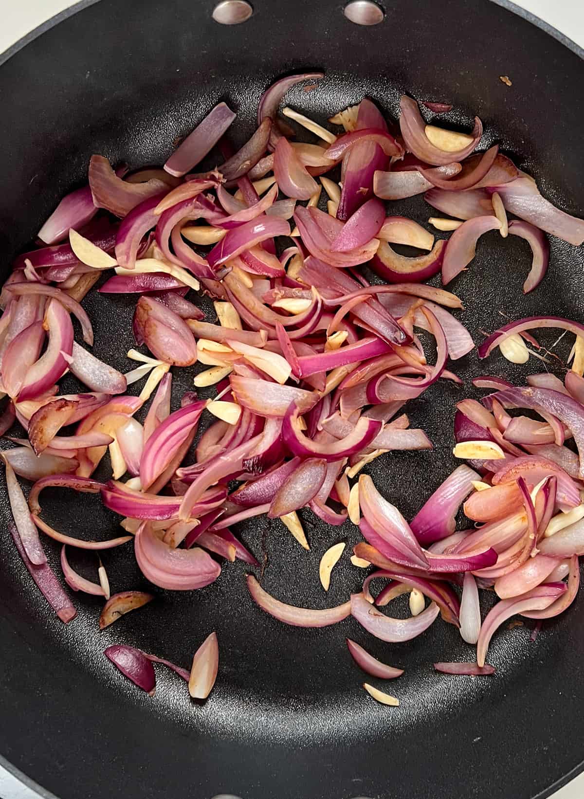 softened red onion slices and garlic slices in a black pan