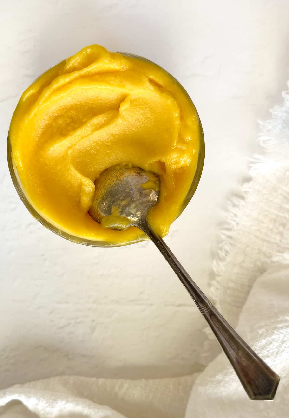 a glass bowl filled with yellow sorbet with a spoon in it