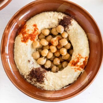 a brown clay bowl filled with blended chickpeas topped with whole cooked chickpeas