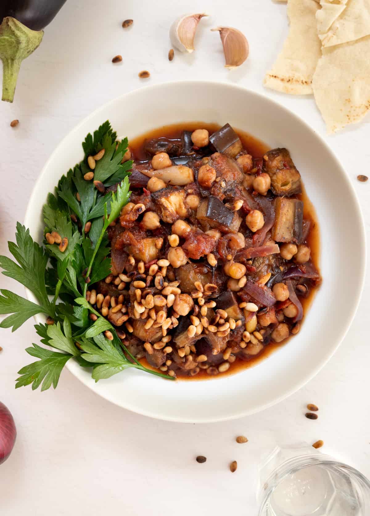 a white round bowl filled with cooked chickpeas and eggplant in a red sauce