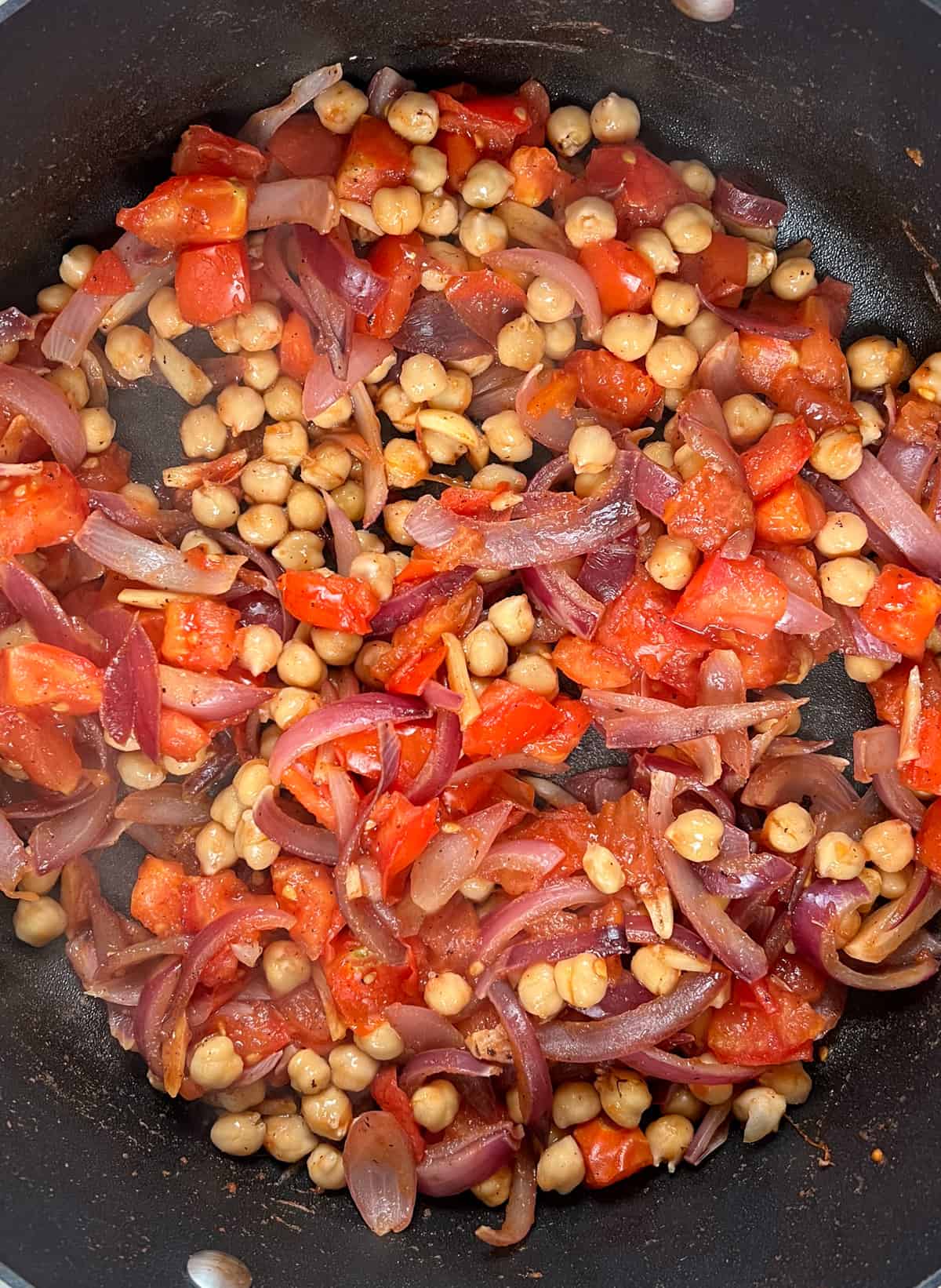 softened diced tomato, chickpeas, red onion slices and garlic slices in a black pan