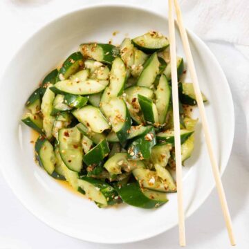 a white plate with chopsticks filled with cucumber and chilli flakes dressing