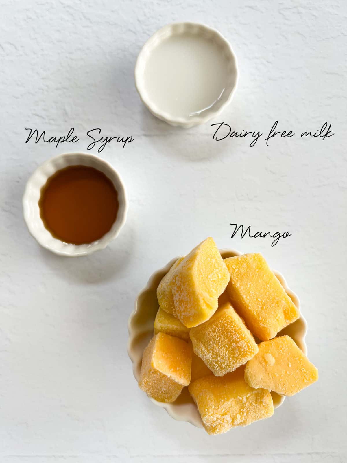 frozen mango, dairy free milk, maple syrup in white bowls