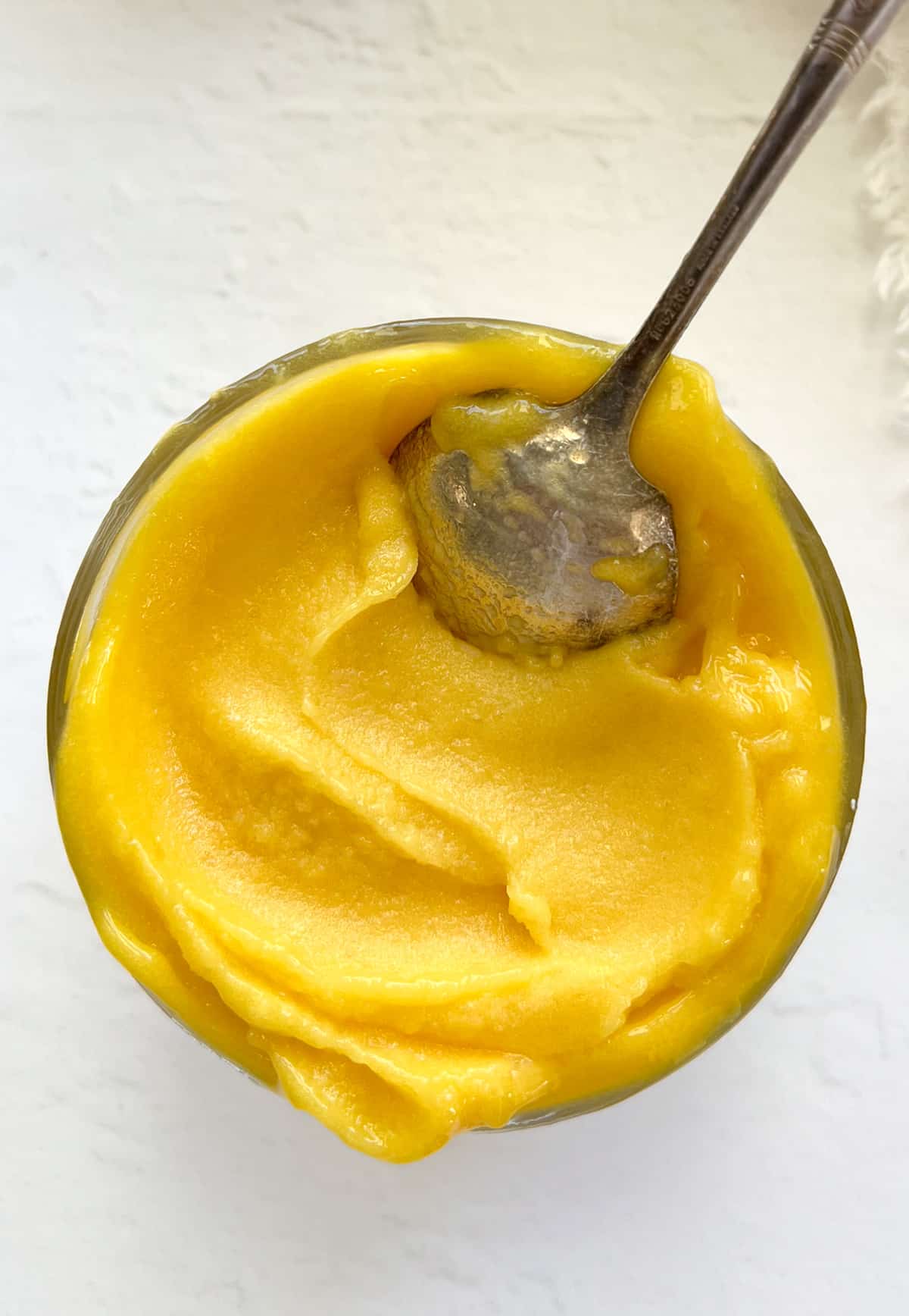 a bowl filled with yellow sorbet and a spoon