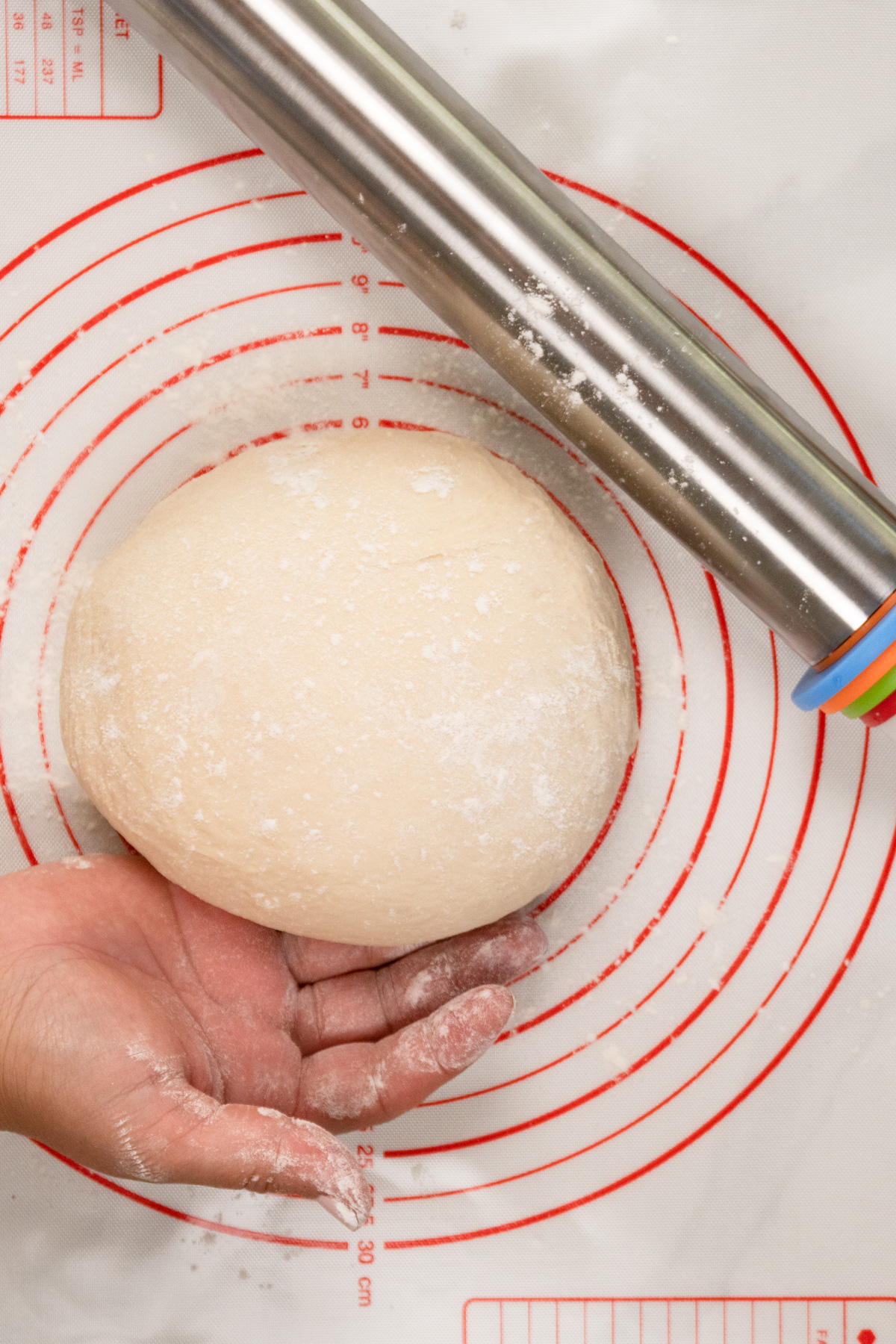 a dough ball held by a hand with a stainless steel rolling pin