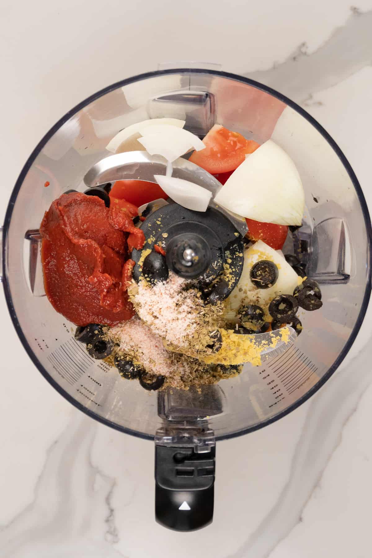 a food processor with red sauce, black olives, onion and yellow flakes