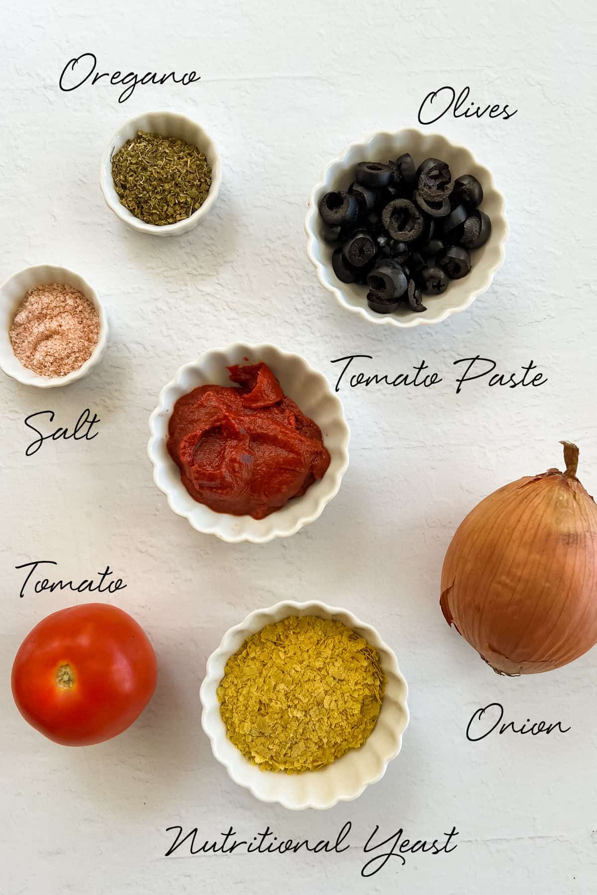 black olives, oregano, onion, nutritional yeast, salt, tomato paste, tomato in white bowls