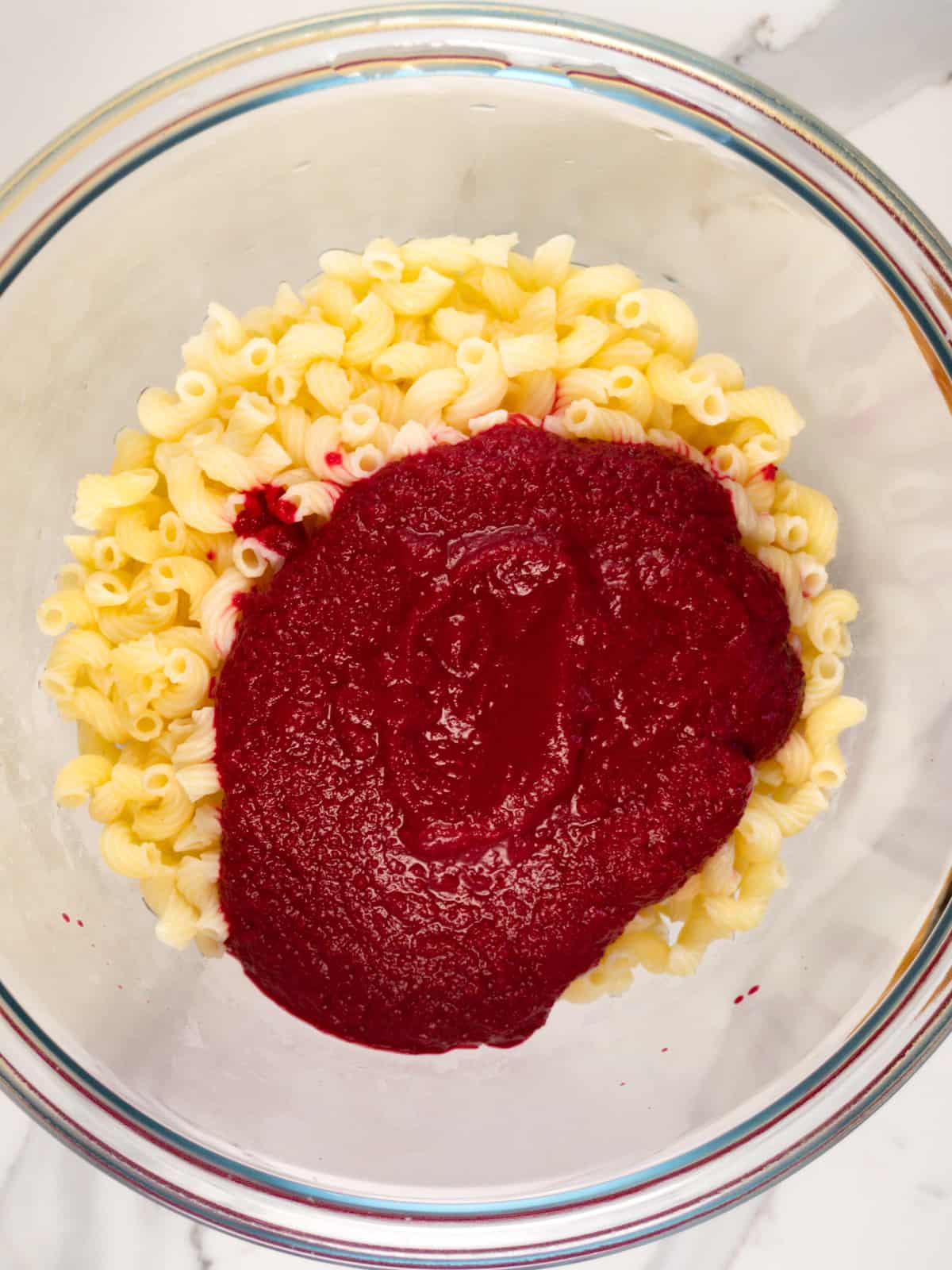 bright pink sauce poured onto cooked elbow pasta in a glass bowl