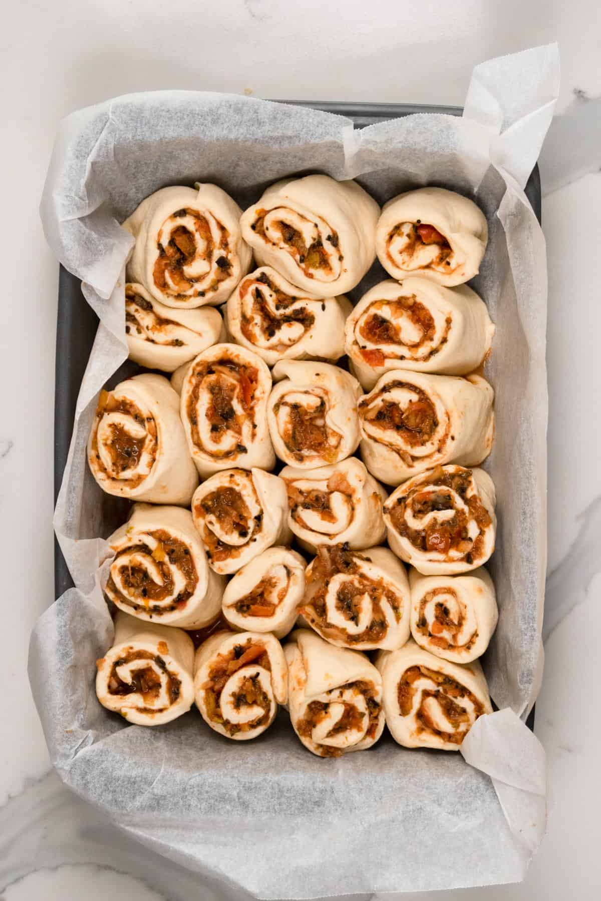 uncooked pinwheels with red sauce in a tray