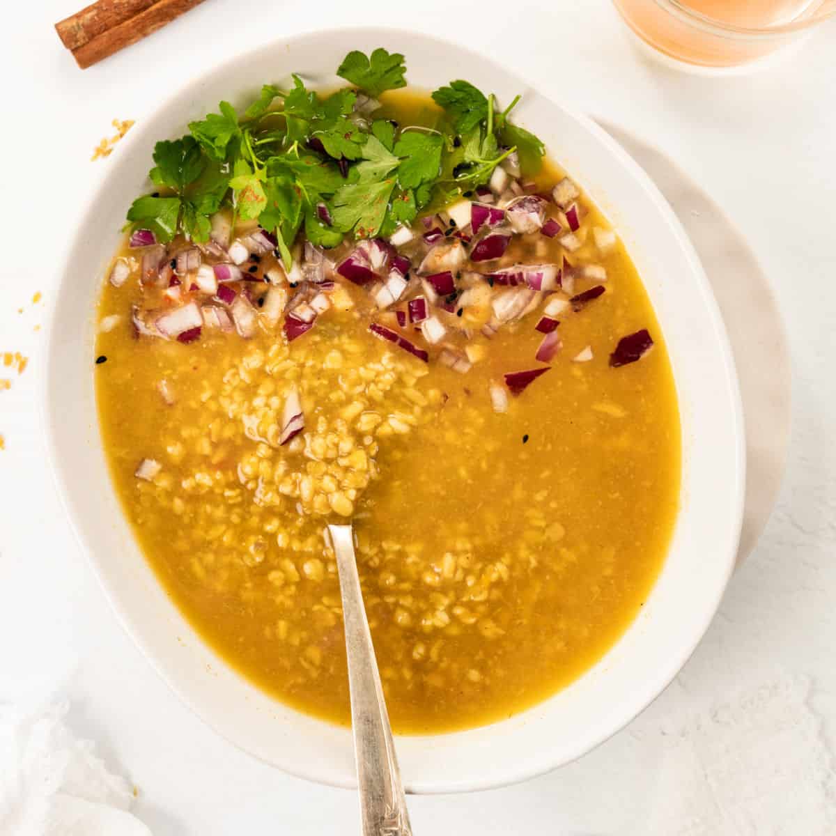 a bowl filled with thick yellow soup, topped with diced red onions and green herbs