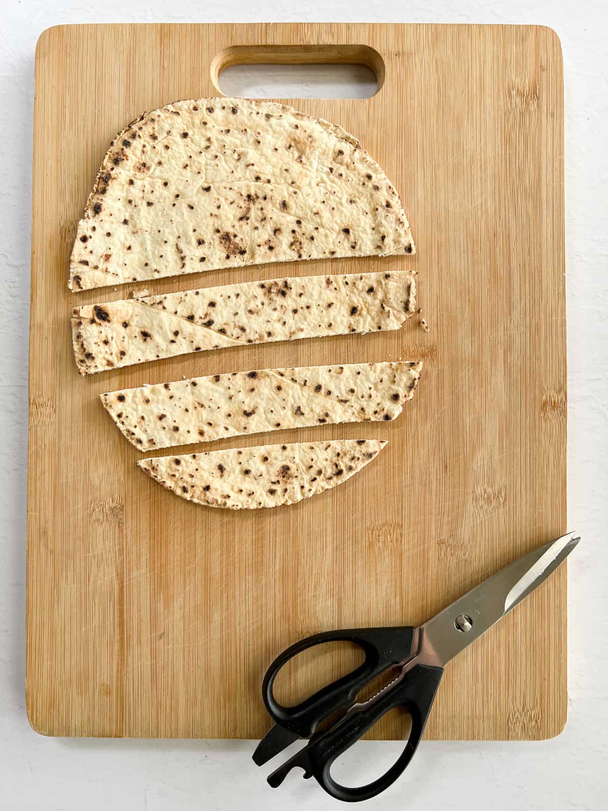 a timber cutting board with kitchen scissors and pita bread cut into strips