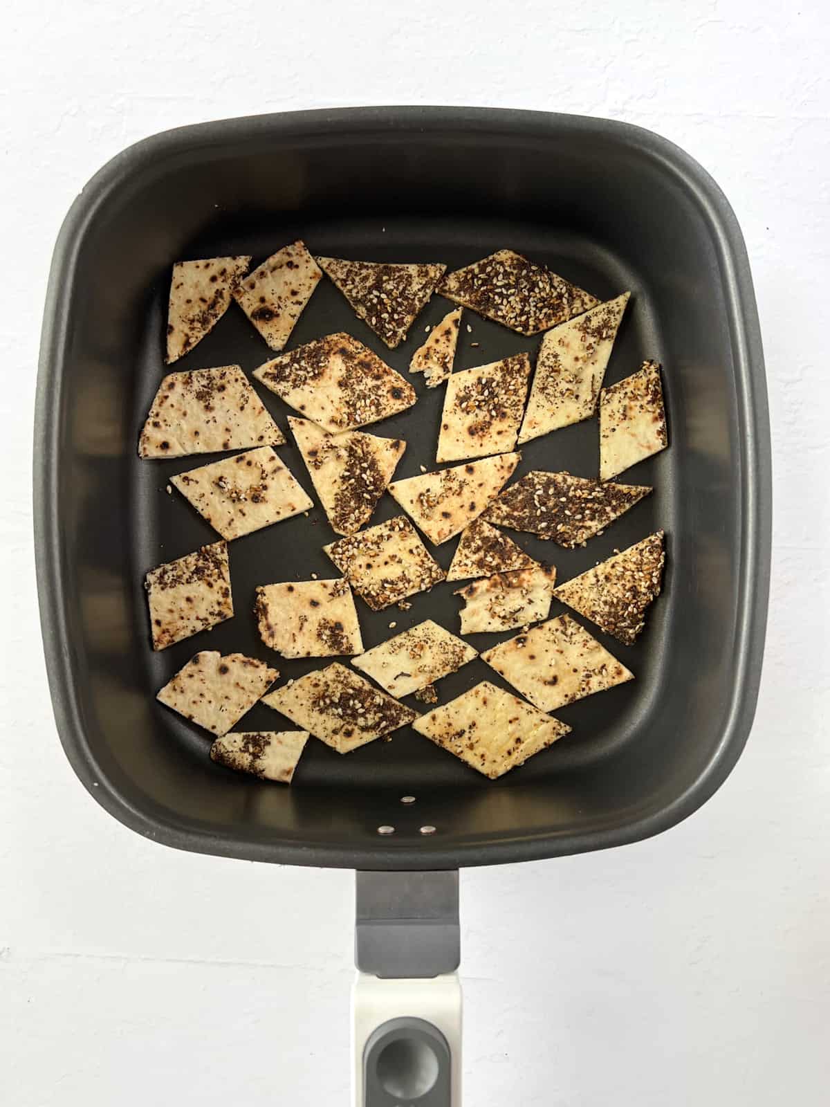 uncooked pita bread pieces coated in seasoning in an air fryer tray