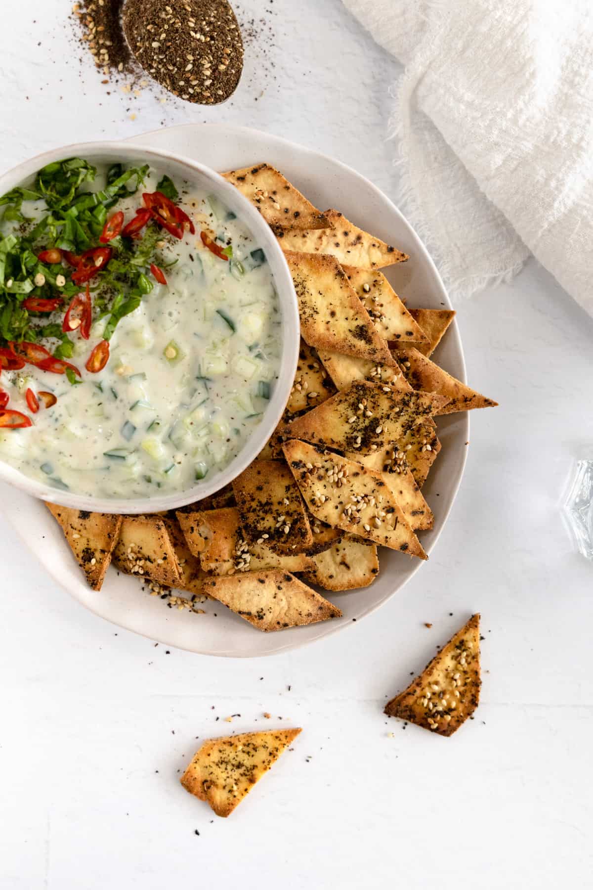 a white bowl with white yogurt cucumber dip and pita chips on the side
