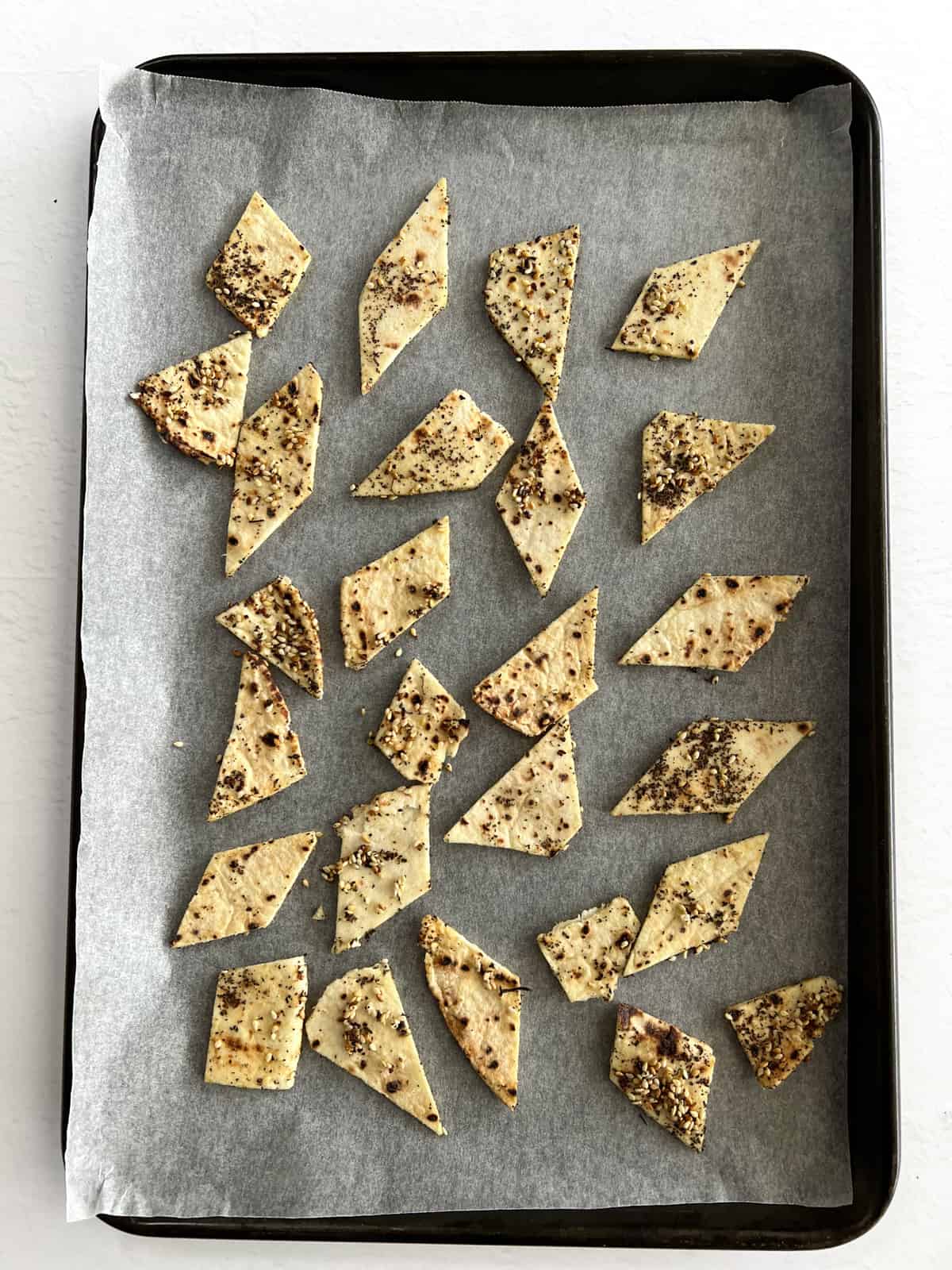 unbaked seasoned pita bread pieces on a white paper lined baking tray