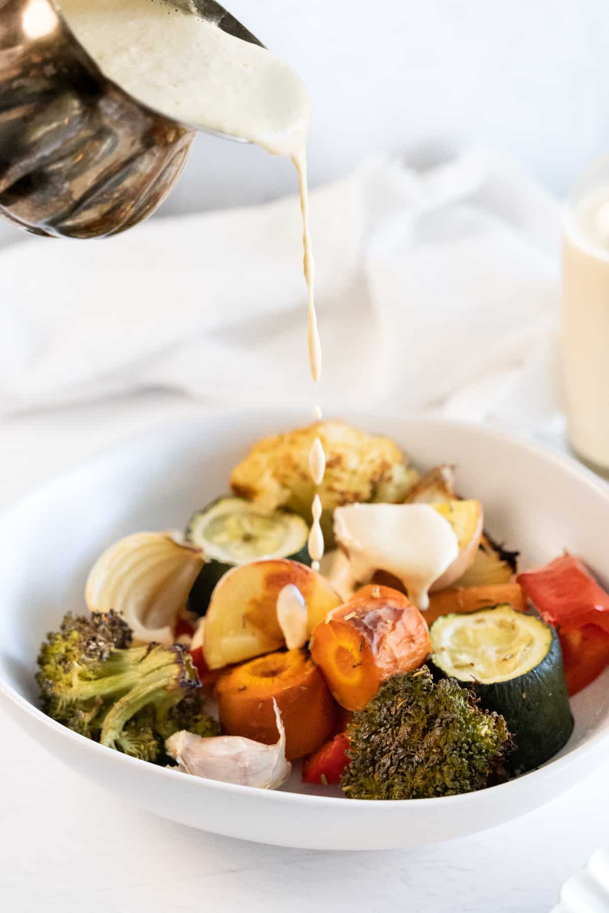 a whiteish sauce being poured over roasted vegetables