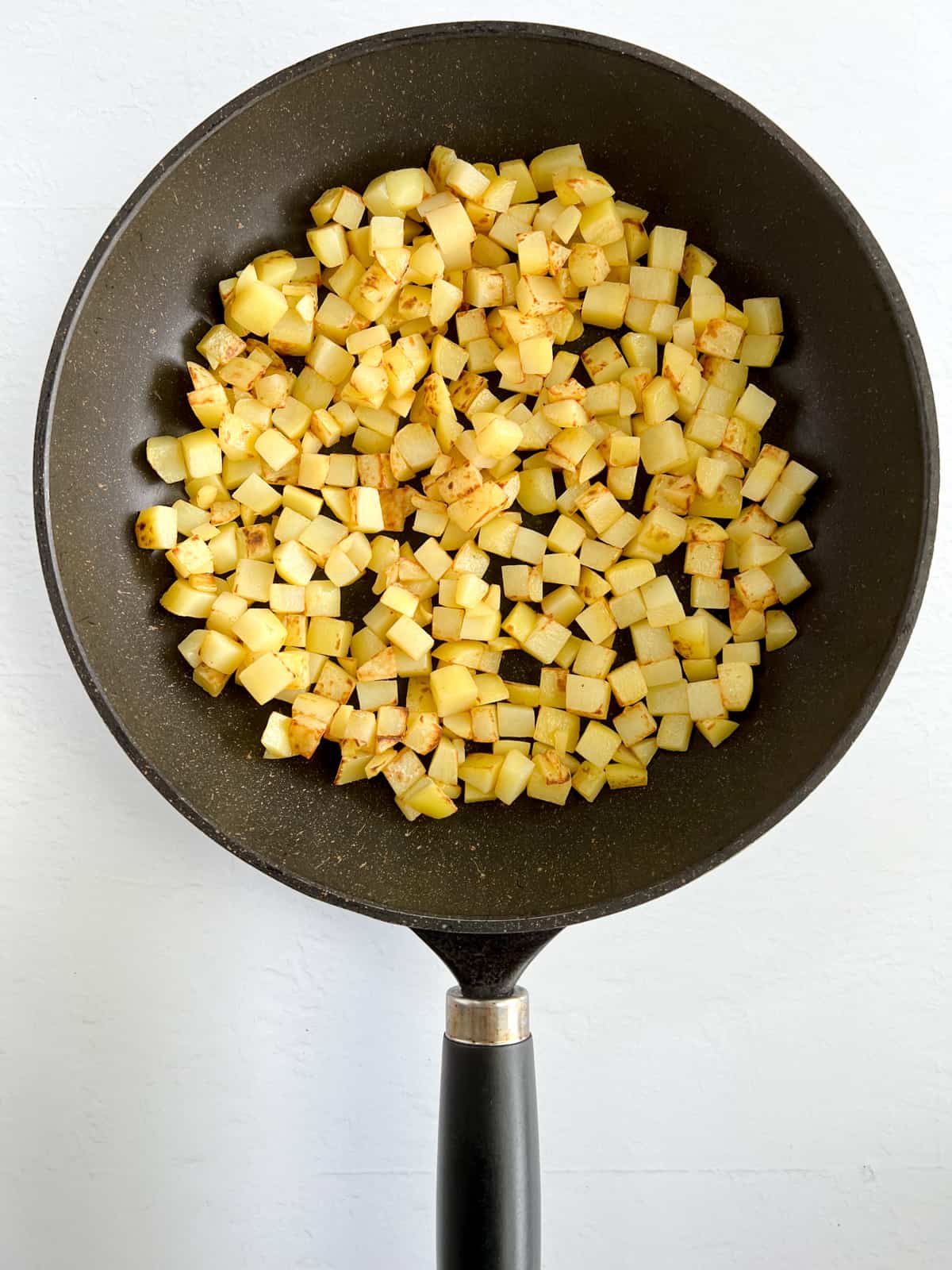 pan fried golden cubed potatoes in a black fry pan