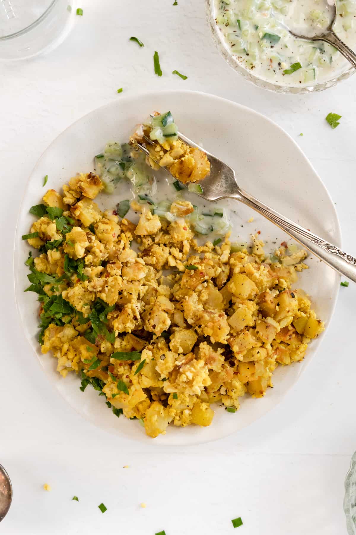 a white plate with a fork and scrambled tofu and diced golden potatoes