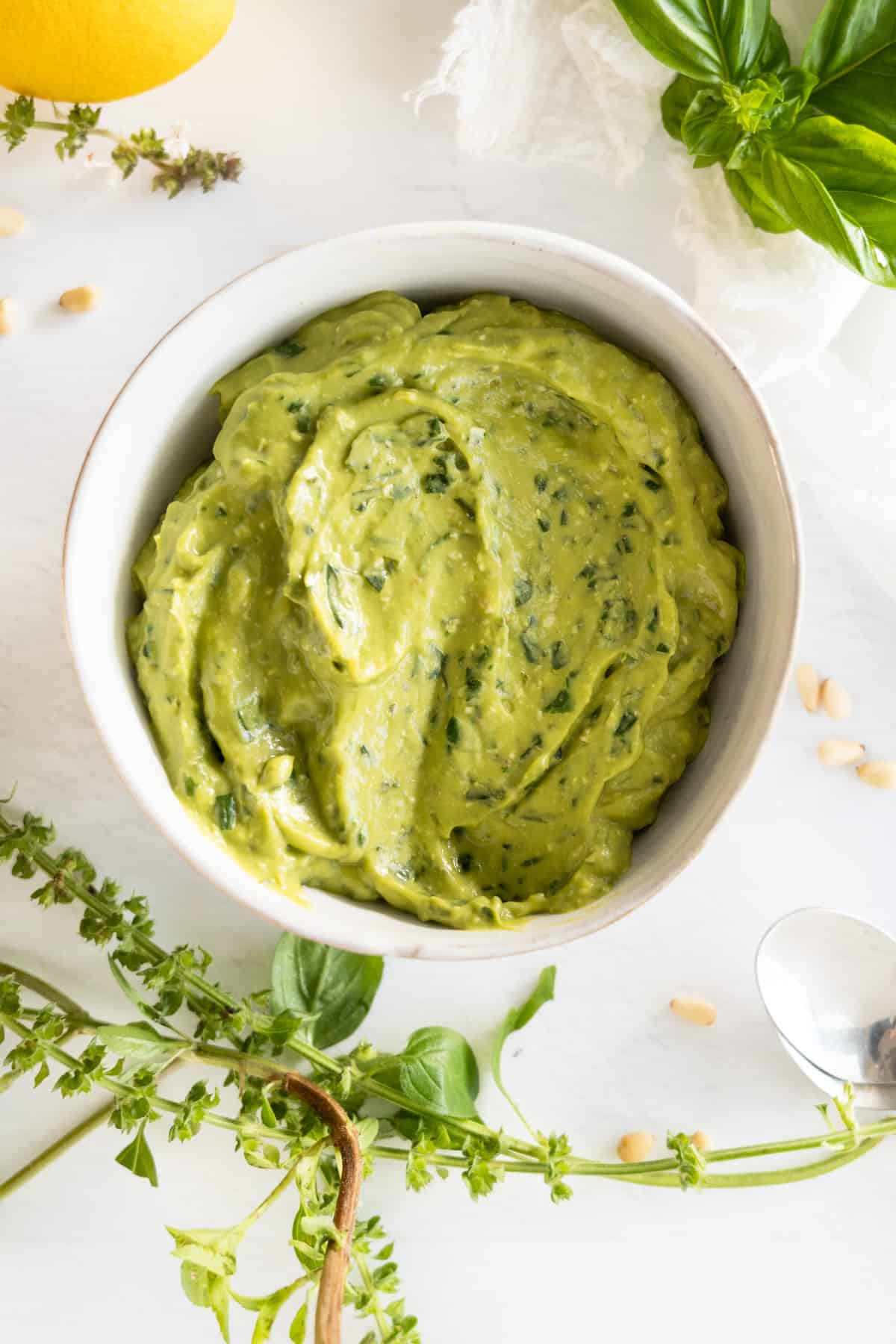 a white bowl with a thick green dressing and basil flowers around it