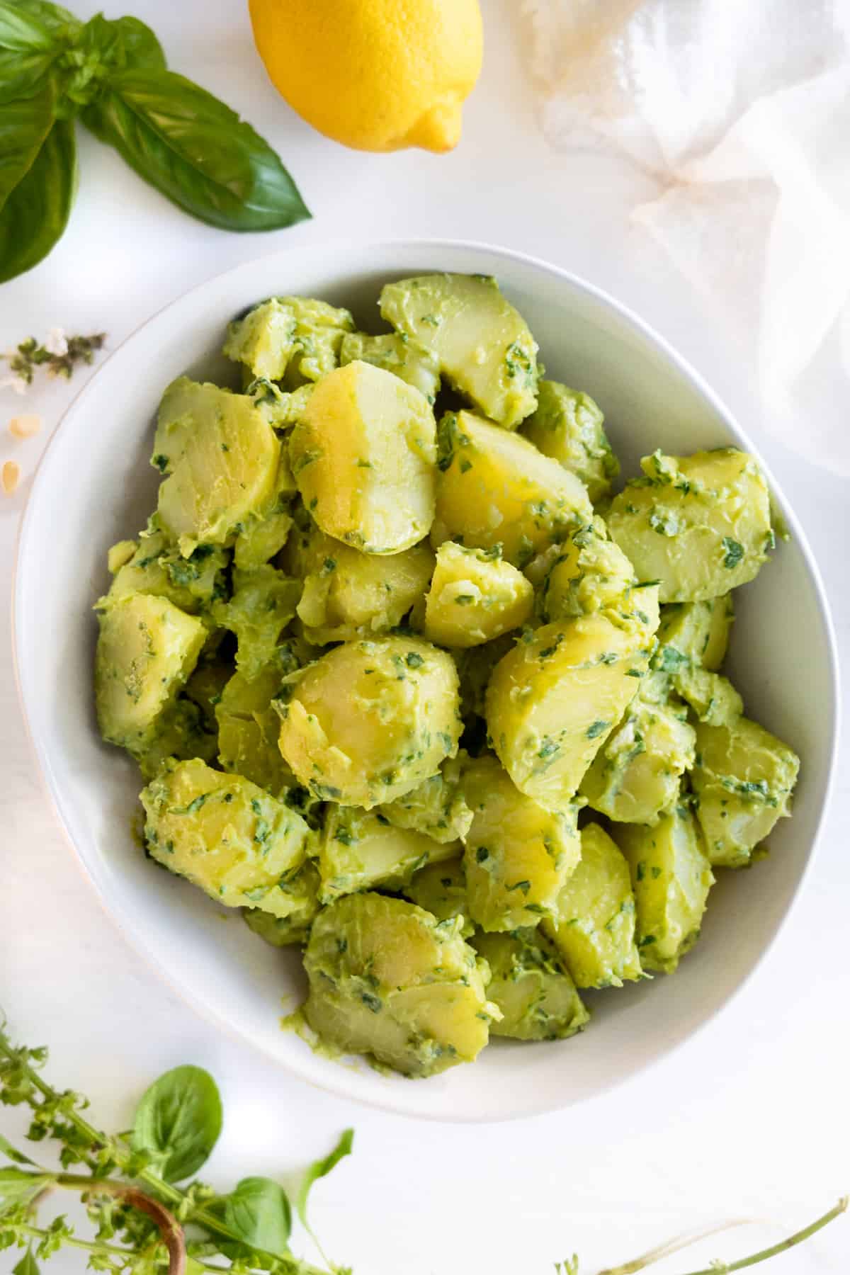 boiled potato pieces tossed in a green sauce in a white bowl with basil leaves and a lemon on the side