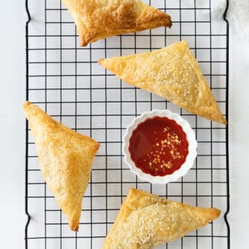 four golden flaky triangle pastries with red sauce in a bowl