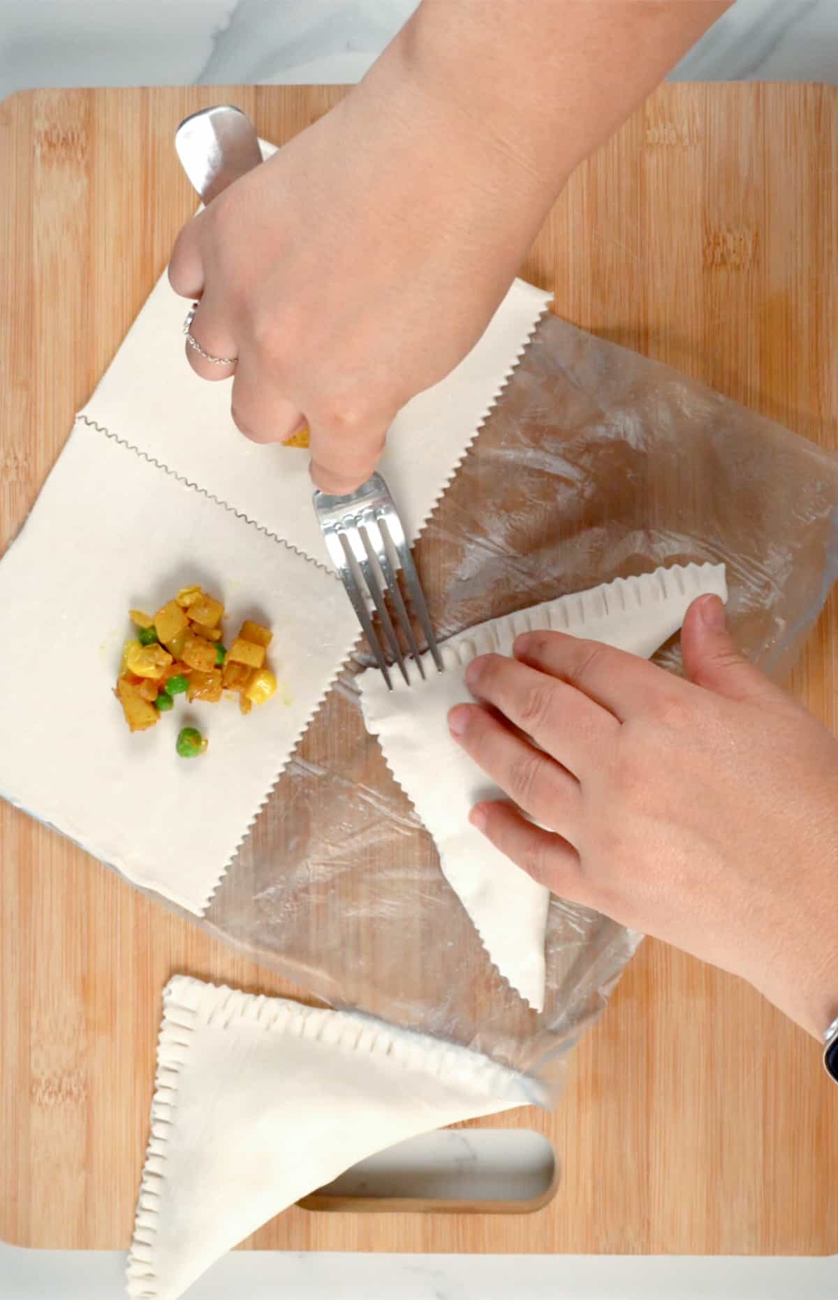 female hands using a fork to seal puff pastry triangles