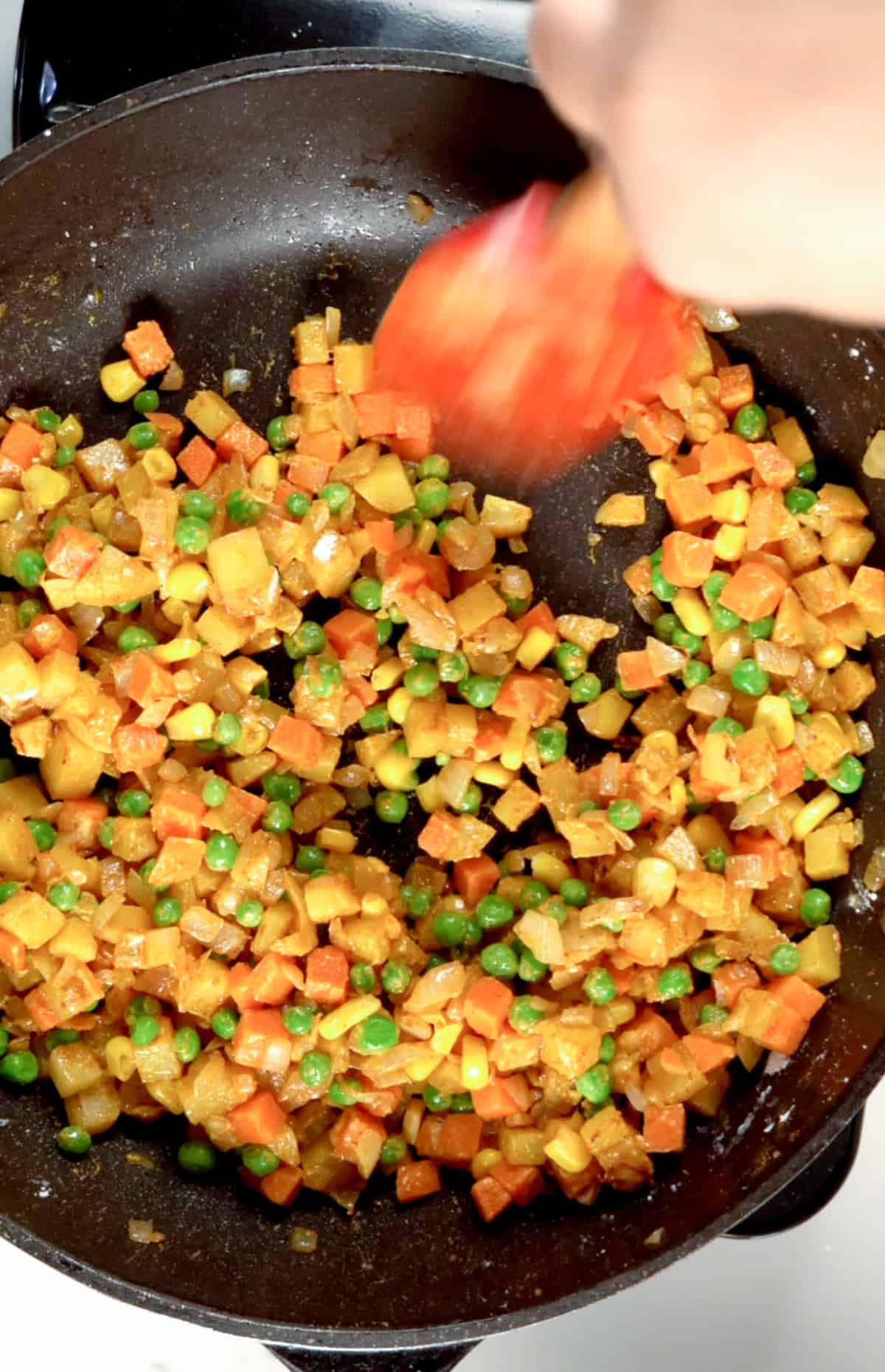 frying carrots, peas, and corn in a black fry pan