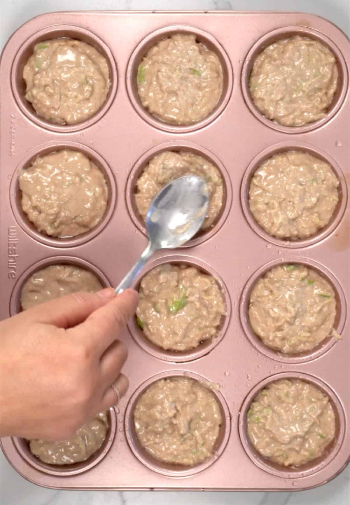 a hand with a spoon flatten out muffin batter in a tray