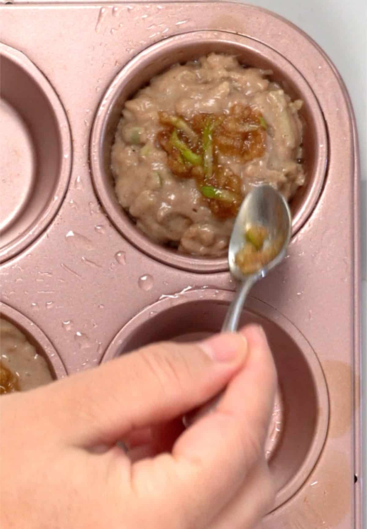 a hand with a spoon adding a brownish topping to muffin batter in a tray