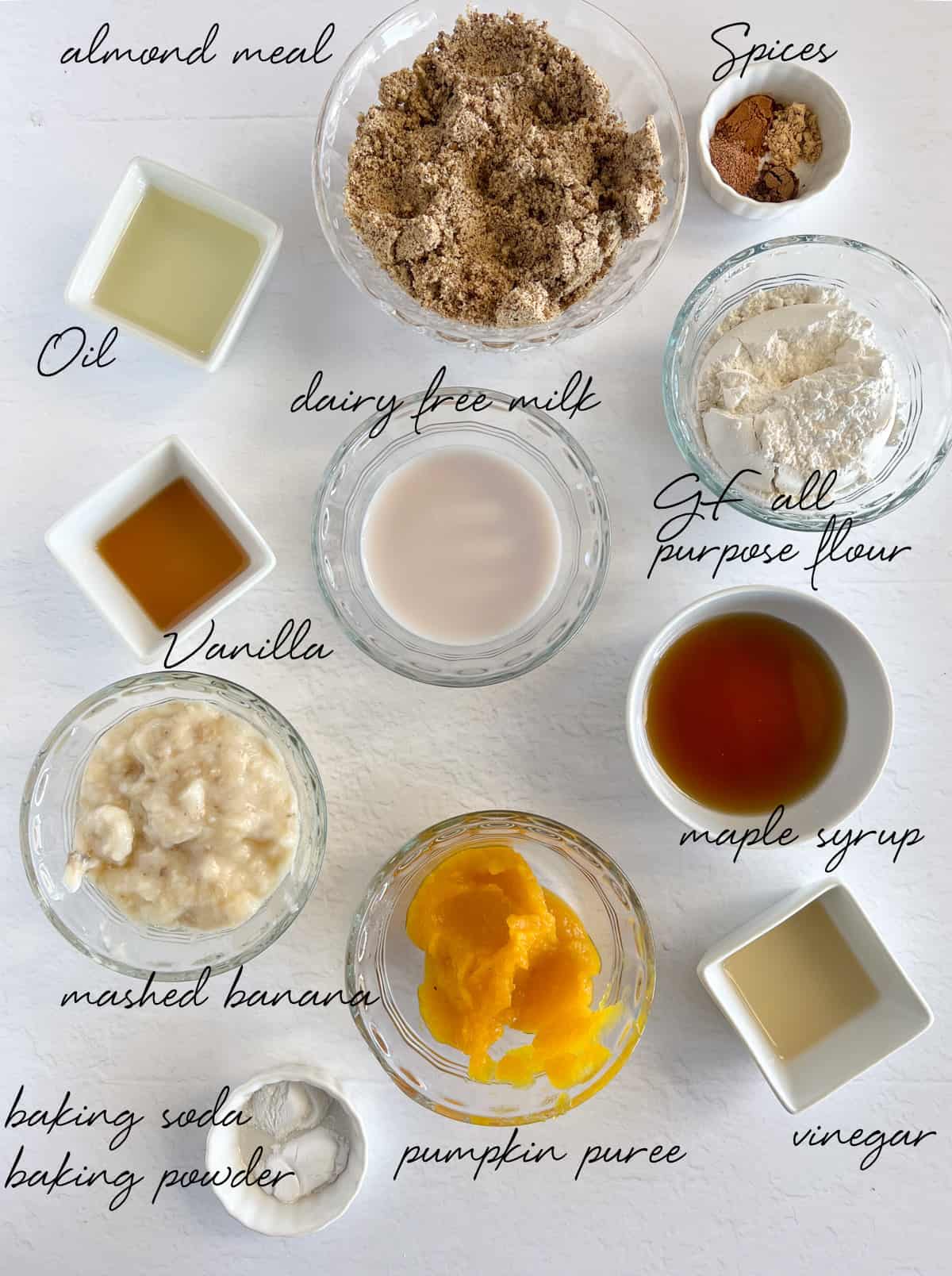 almon meal, oil, spices, flour, maple syrup, pumpkin puree, mashed banana, baking soda and powder, vinegar, vanilla and milk in bowls