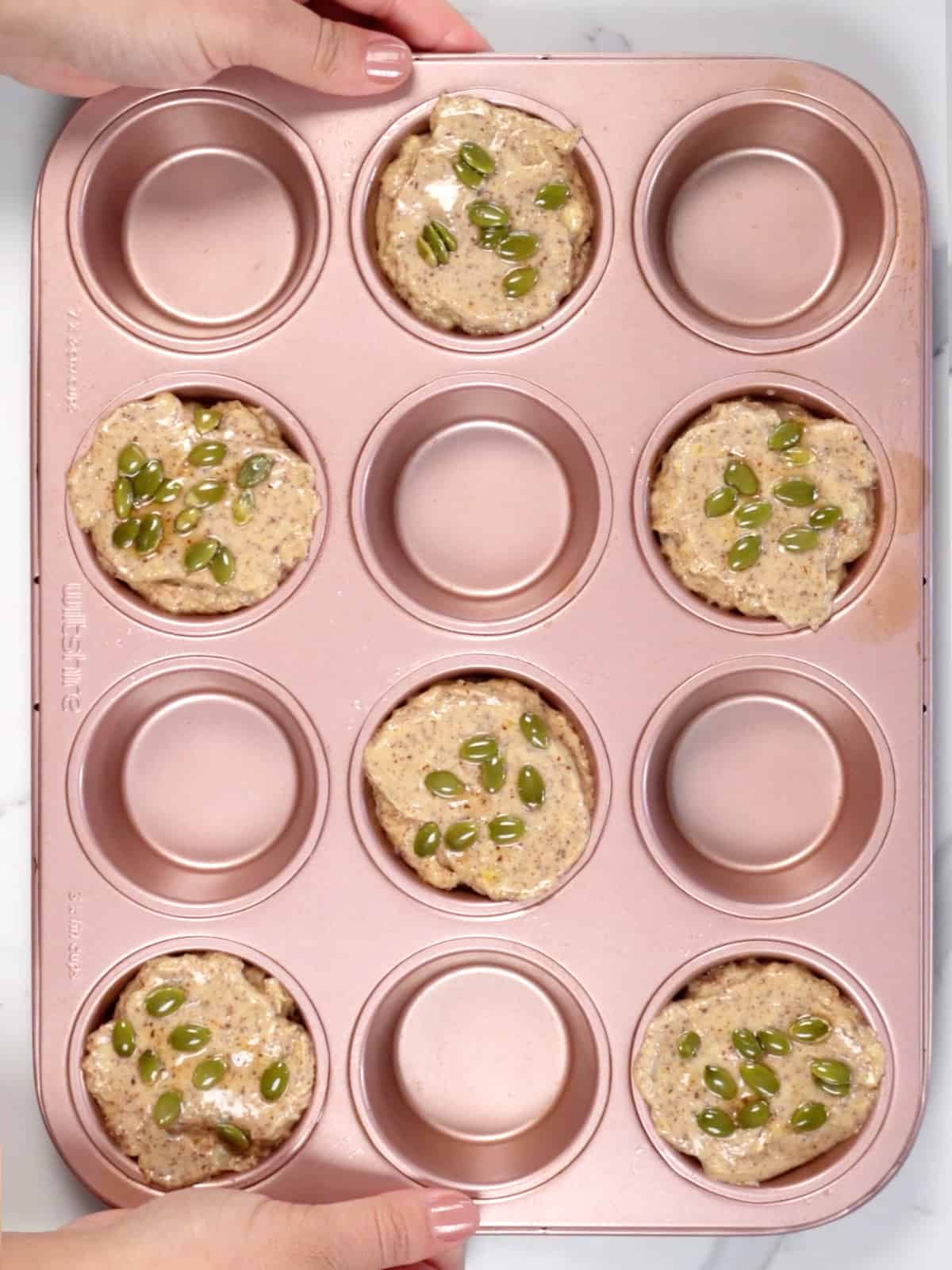 a pink muffin tray with 6 of the muffin cups filled and topped with seeds
