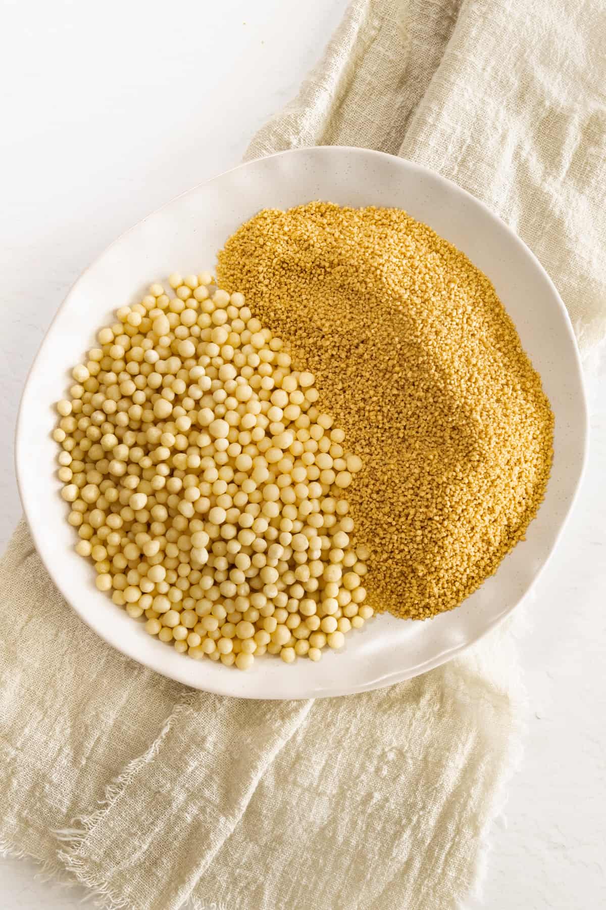 a white plate with small and large dry uncooked couscous