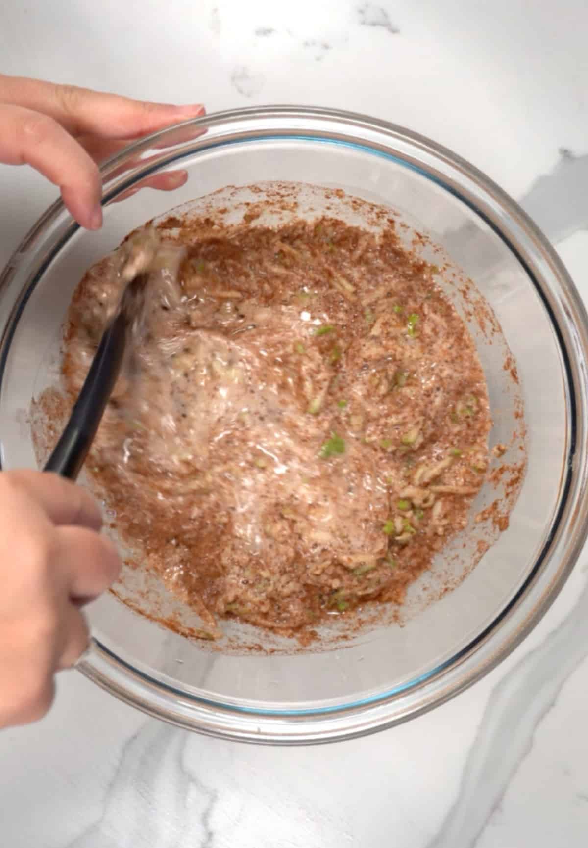 a hand mixing brownish wet ingredients in a glass bowl