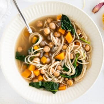 A white bowl filled with vermicelli noodles, chickpeas, spinach and diced carrot soup