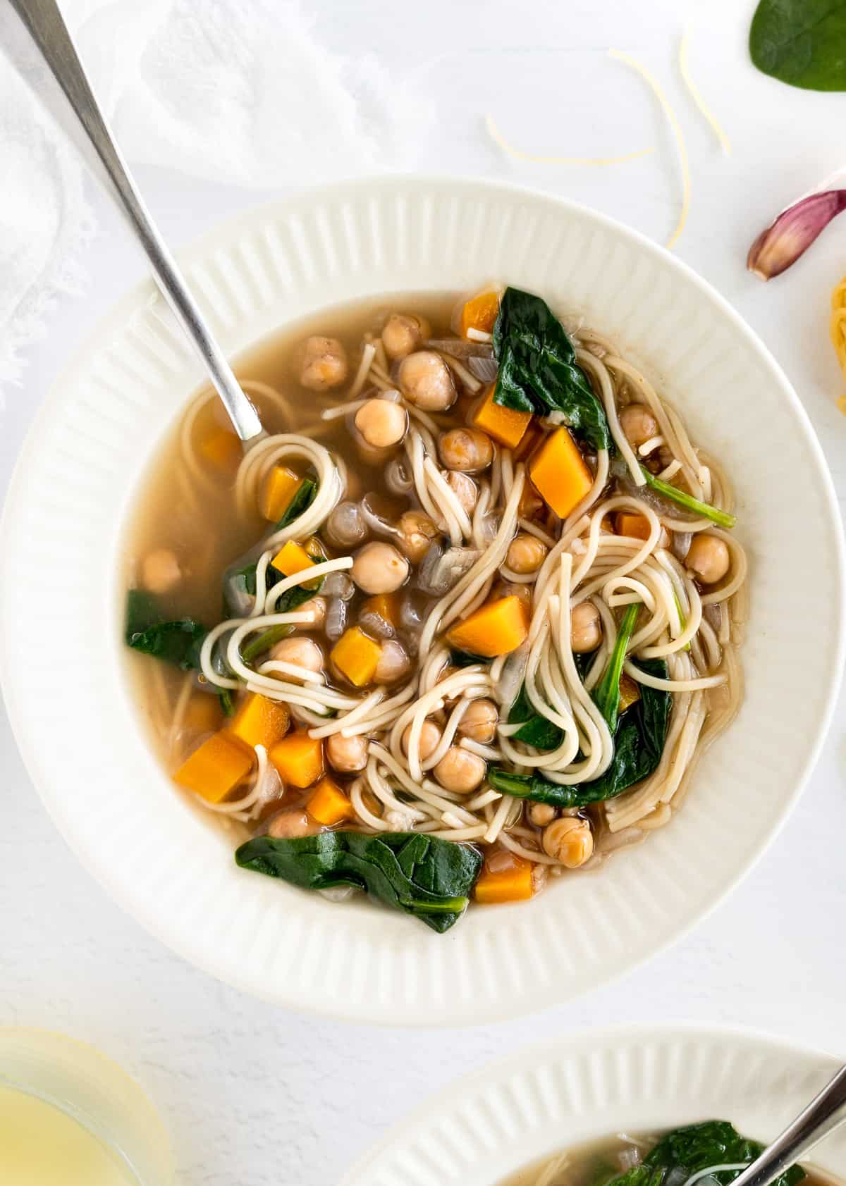 A white bowl filled with vermicelli noodles, chickpeas, spinach and diced carrot soup