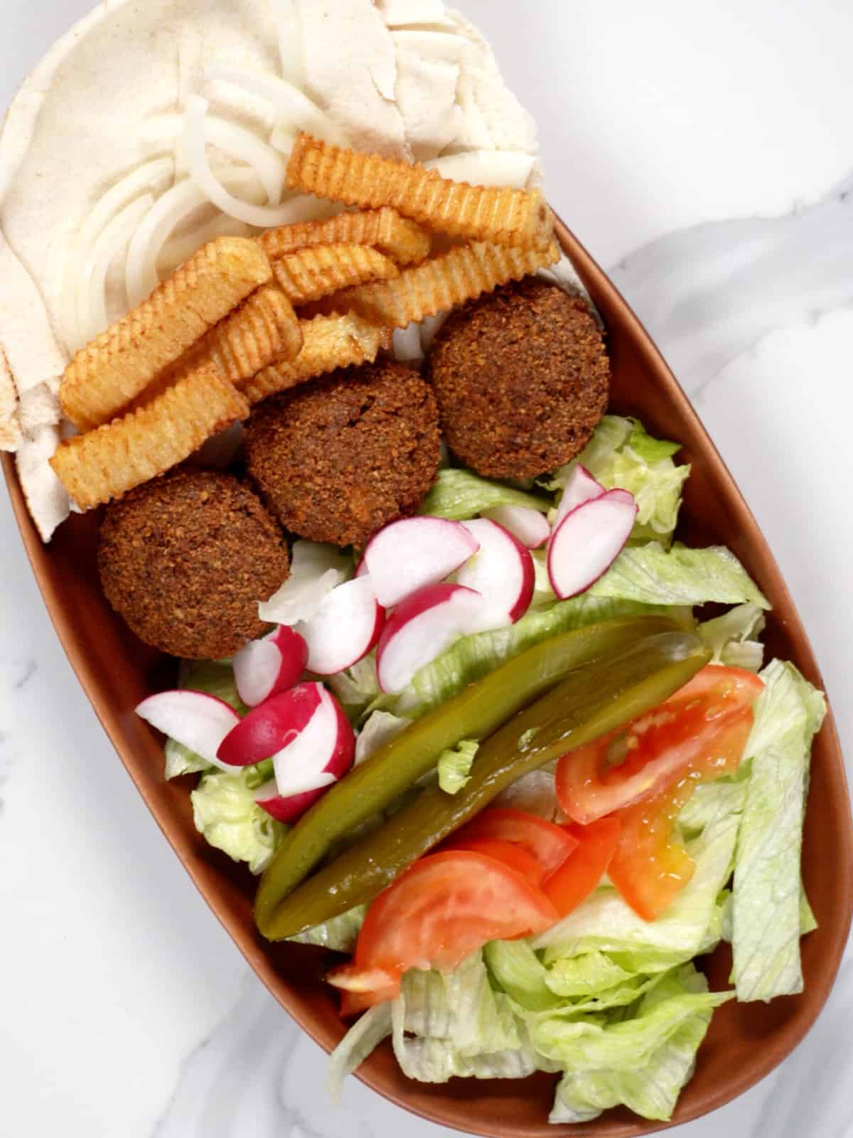 falafel, chopped vegetables, fries and pita bread in a bowl