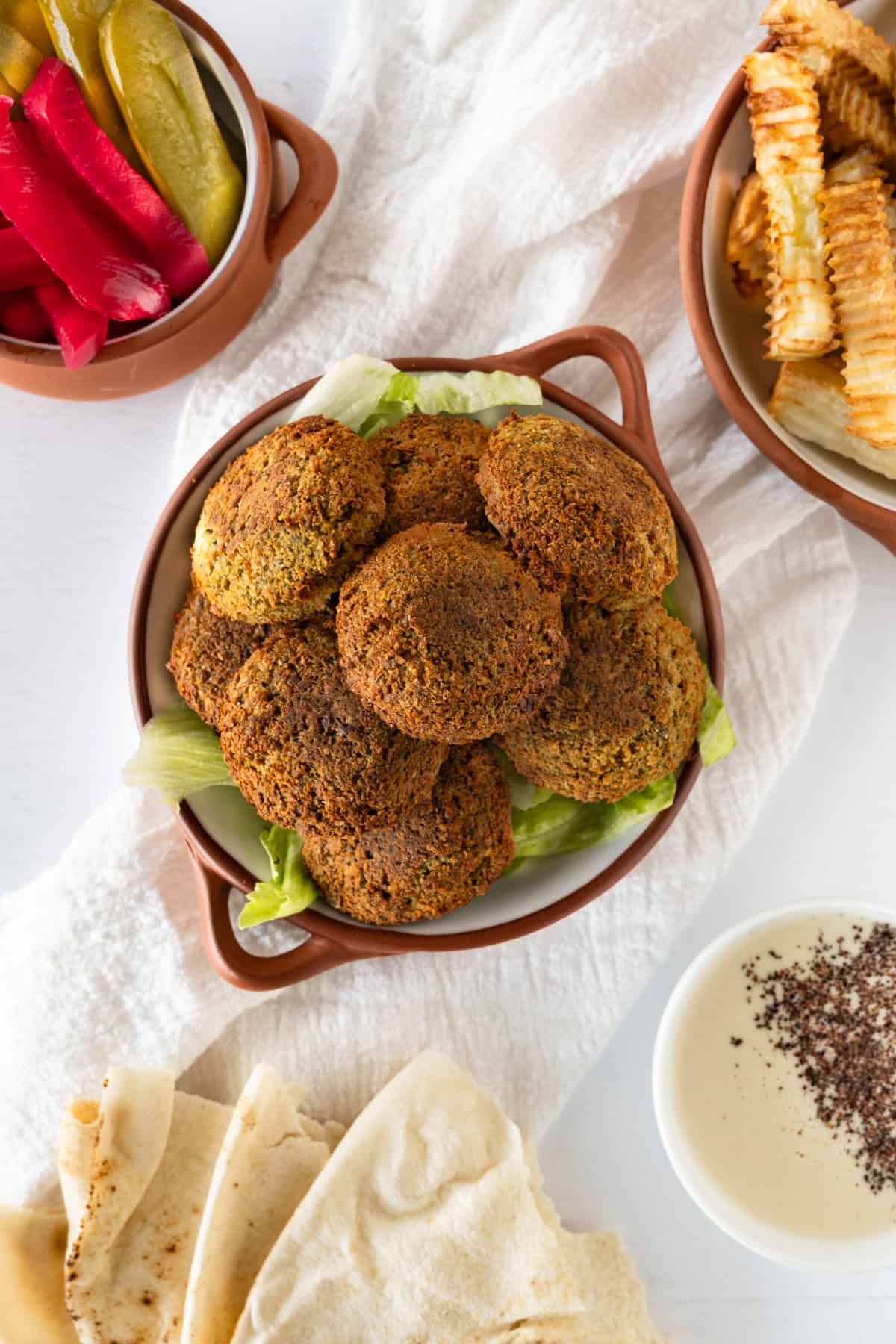 a bowl of golden falafels with a side of pickles, fries and pita bread