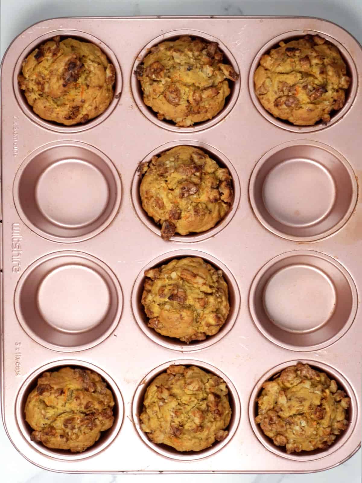 8 baked golden muffins topped with chopped walnuts in a pink muffin tray